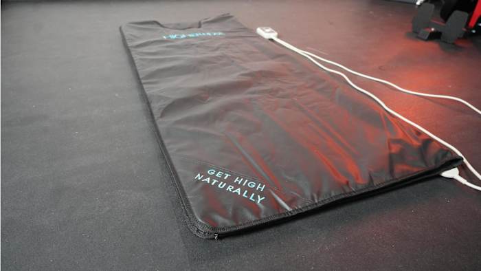 Image of black Higherdose Infrared Sauna Blanket laid out on a black floor with blue text that reads "get high naturally"